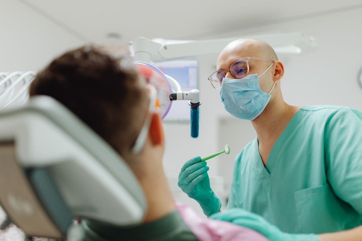 A clinician in a mask calmly attending to a patient in the treatment chair
