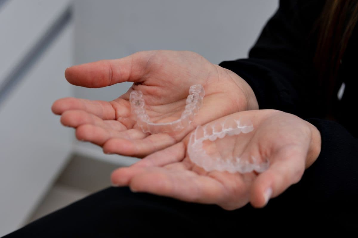 Two clear aligner trays held in open hands
